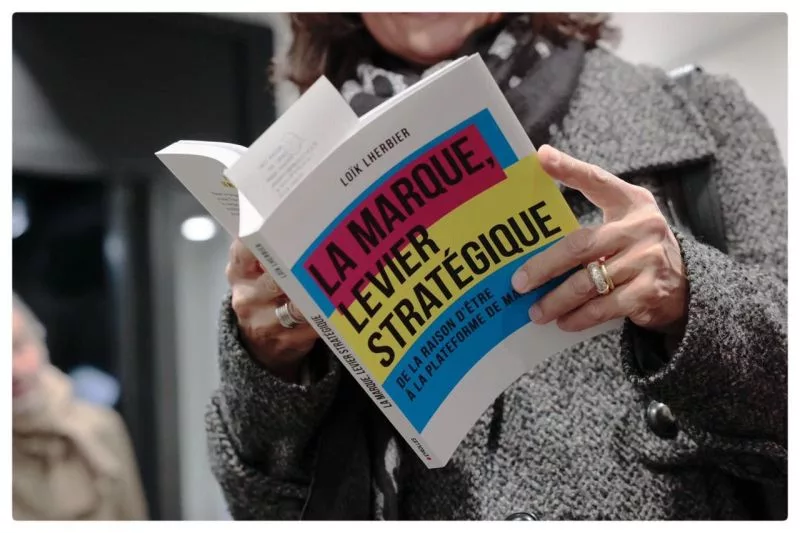 Une lectrice tient en main le livre de Loïk Lherbier, la marque, levier stratégique